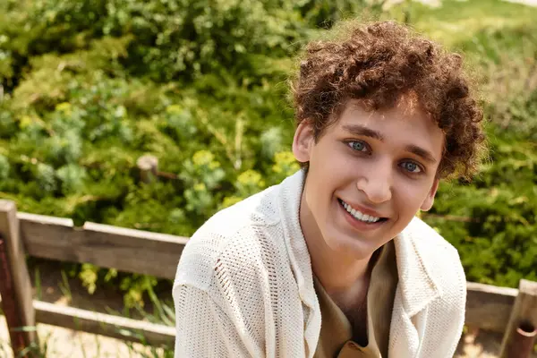 Kıvırcık saçlı genç adam, lüks bir parkta rahat rahat güneşleniyor..