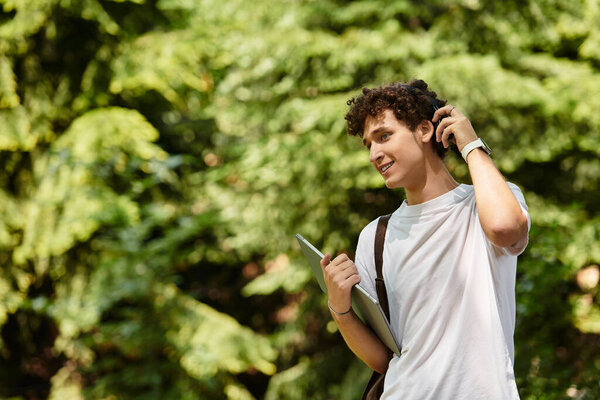 A young man with curly hair is casually spending time outdoors in a lush green park.