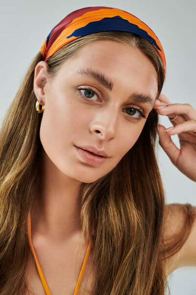 A stylish young woman with tan skin wears a headscarf, expressing summer vibes with natural beauty.