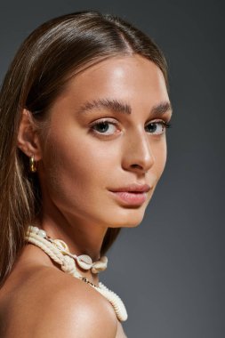 Genç bir kadın doğal makyaj ve deniz kabuğu kolyesiyle parıldıyor, yaz havasını yakalıyor..