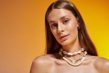 Genç kadın, deniz kabuğu kolyesiyle süslenmiş, sıcak bir yaz elbisesi içinde zarifçe poz veriyor..