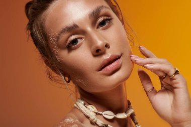 Genç bir kadın yaz tarzını bir deniz kabuğu kolyesi ve stüdyoda parlak ten renginde sergiliyor..