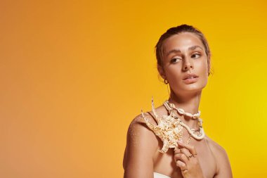 Çekici genç bir kadın canlı bir stüdyoda deniz kabuğu kolyesiyle yaz stilini sergiliyor..