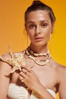 Genç bir kadın yaz elbisesi ve deniz kabuğu aksesuarlarıyla parlıyor..