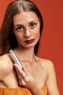 Genç bir kadın, sıcak bir arka planda parlak gümüş bir parfüm şişesiyle cazibesini yayar..