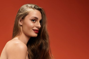 Çekici bir kadın zarif poz verir, uzun saçları ve ışıl ışıl gülüşü cesur bir fon karşısında göz kamaştırır.