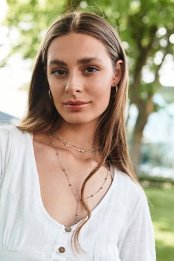 Genç bir kadın yemyeşil bir ortamda zarifçe gülümsüyor, kendine güven ve sıcaklık saçıyor..