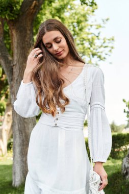 Genç bir kadın ağaçlarla çevrili güneşli, yemyeşil bir yerde zarif bir şekilde duruyor..