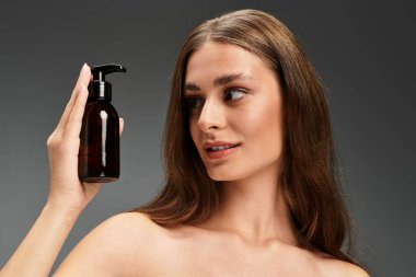 Genç, güzel bir kadın bir deri şişesi tutuyor ve kendinden emin bir şekilde gülümsüyor..