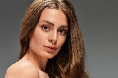 Zarif genç kadın poz veriyor, kusursuz cildini ve yumuşak ışıkta anlamlı bakışlarını vurguluyor..