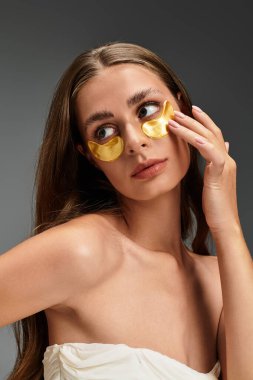 Uzun saçlı genç kadın, çağdaş bir odada dinlenirken altın göz bandı takıyor..