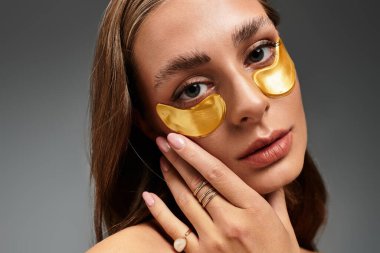 Genç bir kadın altın rengi göz bantlarını takar, kendine bakıcılık rutinini benimser..