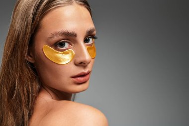 Güzel bir genç kadın, şık bir stüdyo ortamında altın göz bantlarıyla güzelliğini geliştirir..