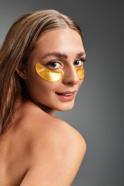 Parlak genç bir kadın, parlak bir stüdyo ortamında altın göz bantları uygularken rahatlıyor.