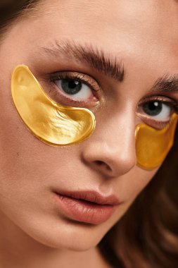 Güzel genç bir kadın, güzellik rutinini altın göz maskeleriyle parlaklık ve tazelik için geliştiriyor.