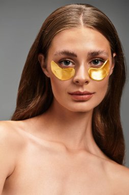 Genç ve güzel bir kadın altın göz bantları takıyor, zarafetle cildini gösteriyor..