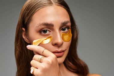 Genç bir kadın altın göz bantlarını kullanarak doğal güzelliğini arttırarak kendine bakmanın tadını çıkarıyor..