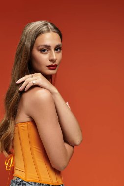 Çarpıcı turuncu elbiseli genç bir kadın uzun saçlarıyla cazibe saçıyor..