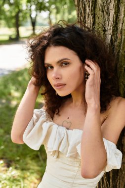 Beyaz yaz elbisesi içinde güzel bir kadın doğanın tadını çıkaran bir ağaca yaslanır..