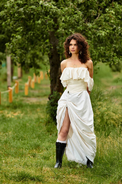 Curly-haired woman enjoys the beauty of a green park while dressed in a flowing summer dress.