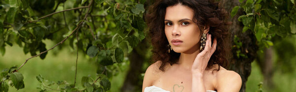 Curly-haired woman in a white summer dress embraces nature in a serene village park, banner