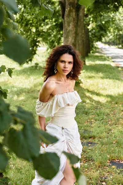 A lovely young woman with curly hair walks through a serene green park, embracing the summer vibes.
