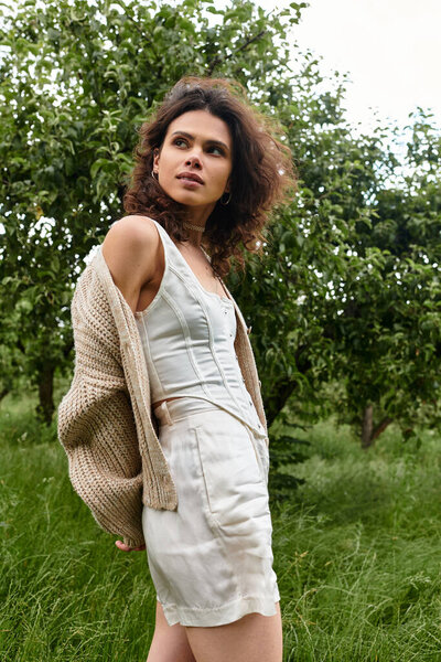 Curly-haired beauty showcases stylish summer fashion in a lush green park setting.