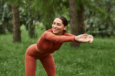 Genç ve güzel bir kadın güneşli bir yoga sırasında yemyeşil alanda zarifçe geriniyor..