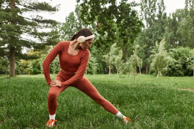 Güneşli bir parkta yoga yapan genç bir kadın odaklanmış enerjisiyle doğayı kucaklıyor..