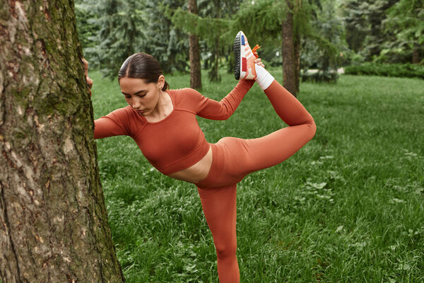 Yoga teacher demonstrates an impressive pose while surrounded by lush greenery and trees.