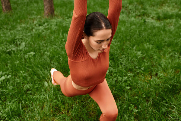 A young beautiful woman demonstrates impressive yoga flexibility in a vibrant green park.