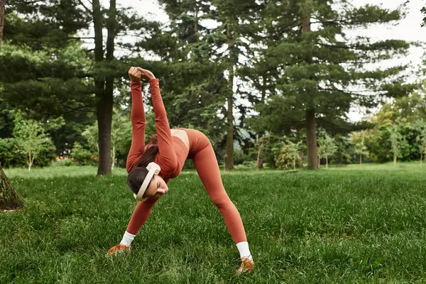 Genç bir kadın yeşil bir parkta yoga yapıyor, atletizmini vurguluyor..