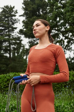 Genç ve güzel bir kadın yemyeşil bir çevrede atlama ipiyle güvenle ayakta duruyor..