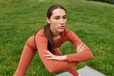 Genç ve güzel bir kadın, yeşil bir tarlada güneşli bir günde zorlu bir yoga pozu veriyor..