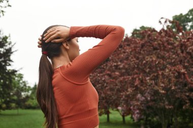Atkuyruklu genç bir kadın canlı yeşillikler ve renkli yapraklar arasında yansıyor..
