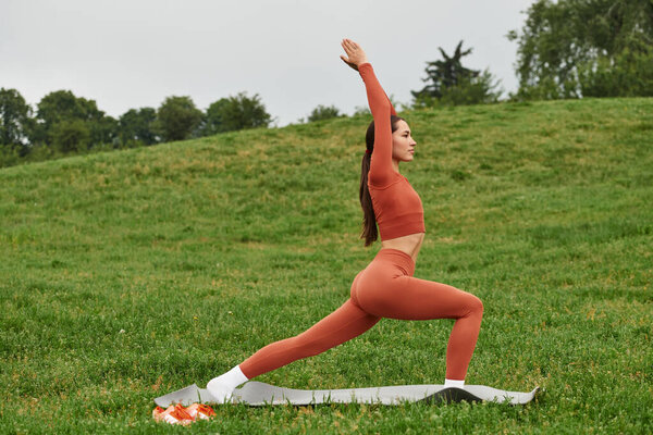 A beautiful yoga teacher engages in a graceful pose amidst lush greenery during early morning light.