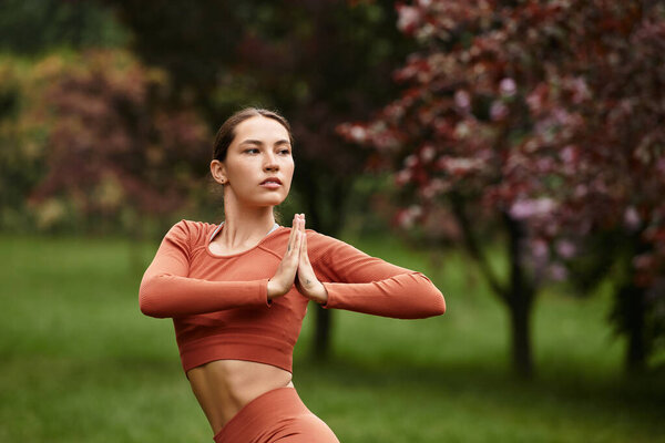 A young woman finds peace practicing yoga among the trees in nature.