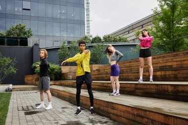 Dört enerjik genç insan hareketli bir şehir ortamında ısınma hareketleri yapıyor..