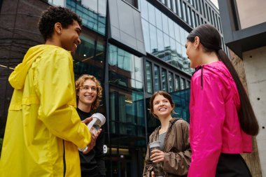 Renkli ceketli dört genç arkadaş içkinin tadını çıkarırken gülüşlerini ve gülüşlerini paylaşıyor..