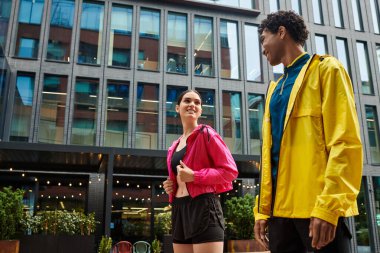 İki sportif birey açık bir gökyüzünün altında spor giysileri içinde sohbet edip gülümsüyor..