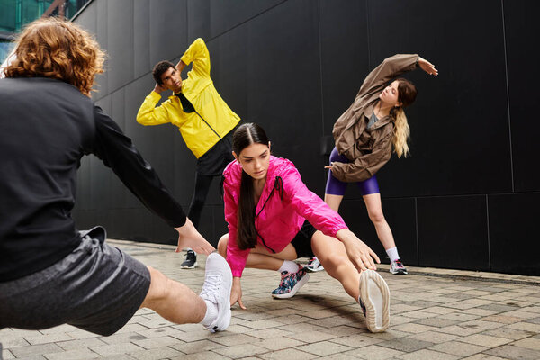 Группа молодых, спортивных людей, занимающихся динамическими упражнениями на растяжку на городском тротуаре.