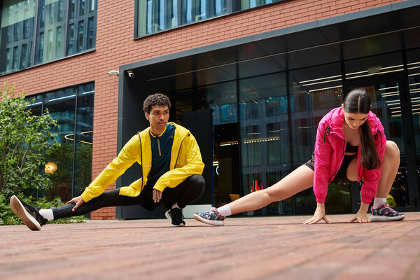 Two sporty individuals perform stretching exercises in a contemporary outdoor area.