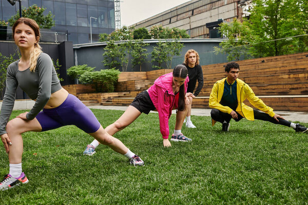 Четыре спортивных лица растягиваются в зеленом парке в окружении городских сооружений в солнечный день