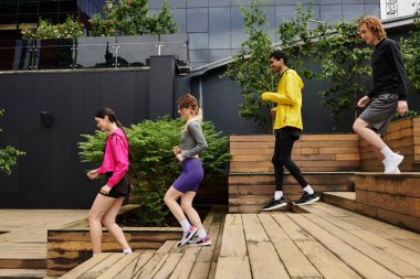 Dört sporcu ahşap merdivenlerden aşağı koşuyor, yemyeşil ortamda spor yapmanın keyfini çıkarıyorlar..