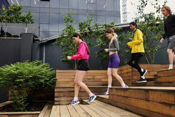Группа атлетических молодых людей спускается по деревянной лестнице среди зелени и современной архитектуры.