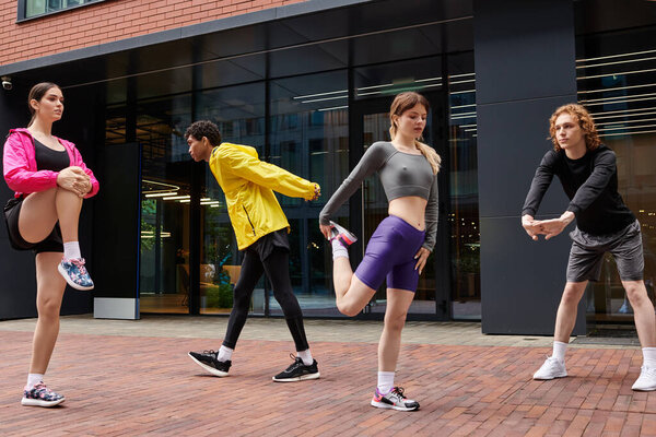 Четыре молодых спортсмена растягиваются и готовятся к тренировкам в динамичной городской среде.