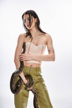 Kendine güvenen genç bir kadın zarif bir şekilde poz veriyor. Koluna bir yılan sarılmış ve güç yayıyor..