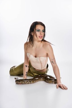 Genç bir kadın, bir yılanla poz veriyor. Güzellik ve tehlikeyi minimalist bir stüdyoda harmanlıyor..