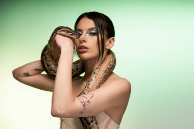 Güzel bir kadın, koluna zarif bir şekilde sarılmış bir yılanla güven içinde poz verir..