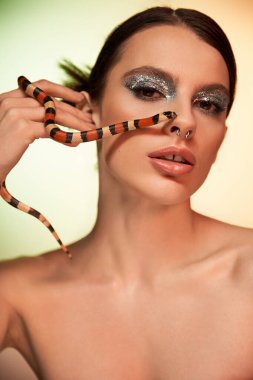 Çarpıcı genç bir kadın cesur bir makyaja ve zarif bir şekilde eline sarılmış bir yılana sahiptir..